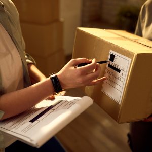 Two delivery women cooperating while checking data on the packages in the office.
